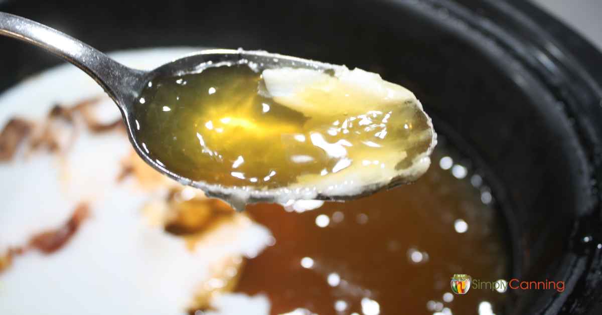Skimming off fat from the ham broth with a spoon.