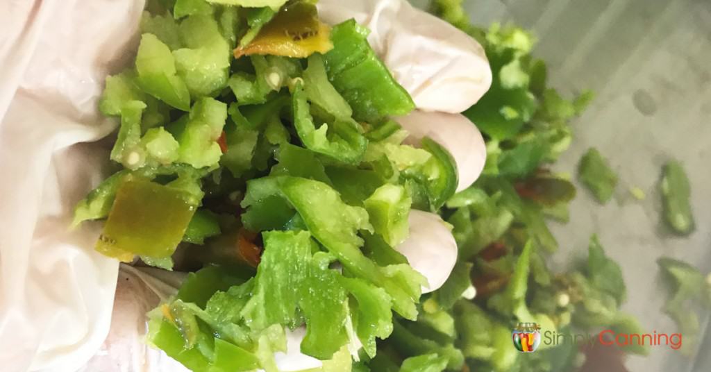 A gloved hand holding green and red peppers that have been chopped into small pieces.