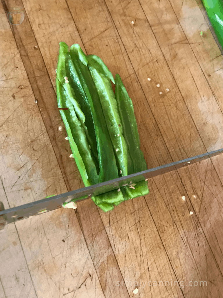 Chopping sliced green peppers into smaller pieces using a sharp knife on a wooden cutting surface.