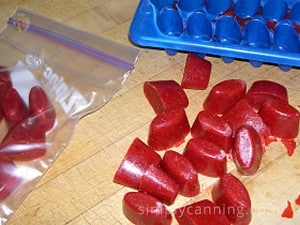 Strawberry ice cubes out on the counter with a blue ice tray, and freezer bag in the background.  