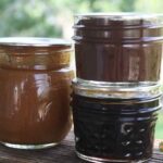 Three small jars of various fruit butters sitting on a railing outdoors.