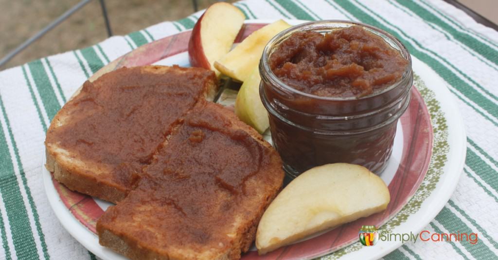 Apple butter on toast with a small jar of apple butter and slices of apples.