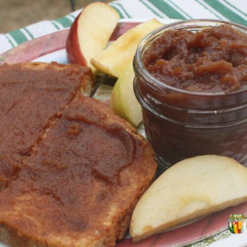 Apple butter on toast with a small jar of apple butter and slices of apples.