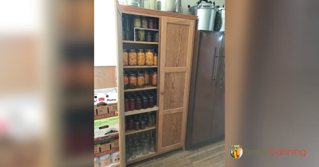 A wooden cabinet with its shelves filled with jars of home canned food.