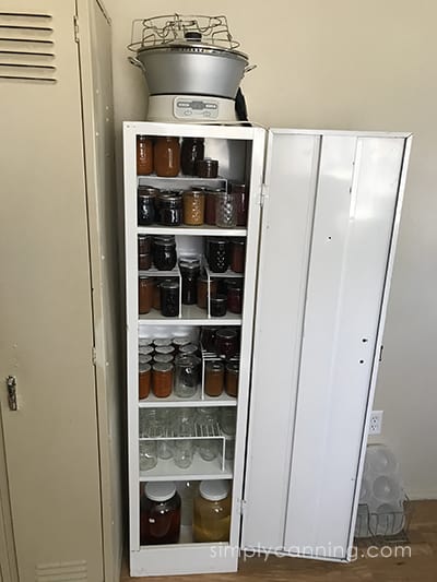 Smaller metal cabinet opened to reveal jars of home canned jams and jellies.