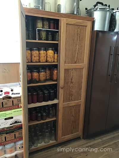 A wooden cabinet filled with jars and jars of home canned food.