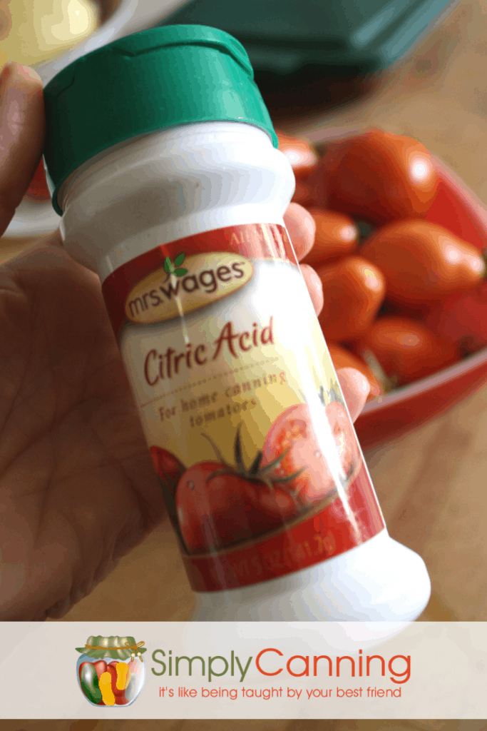 Holding a bottle of citric acid with a bowl of tomatoes waiting in the background.