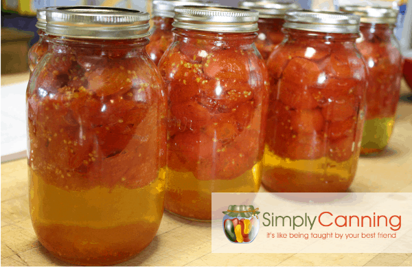 Jars filled with tomatoes that are floating above the tomato liquid inside the jars.