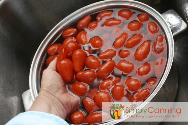 Pulling a handful of red tomatoes out of a pot of water.