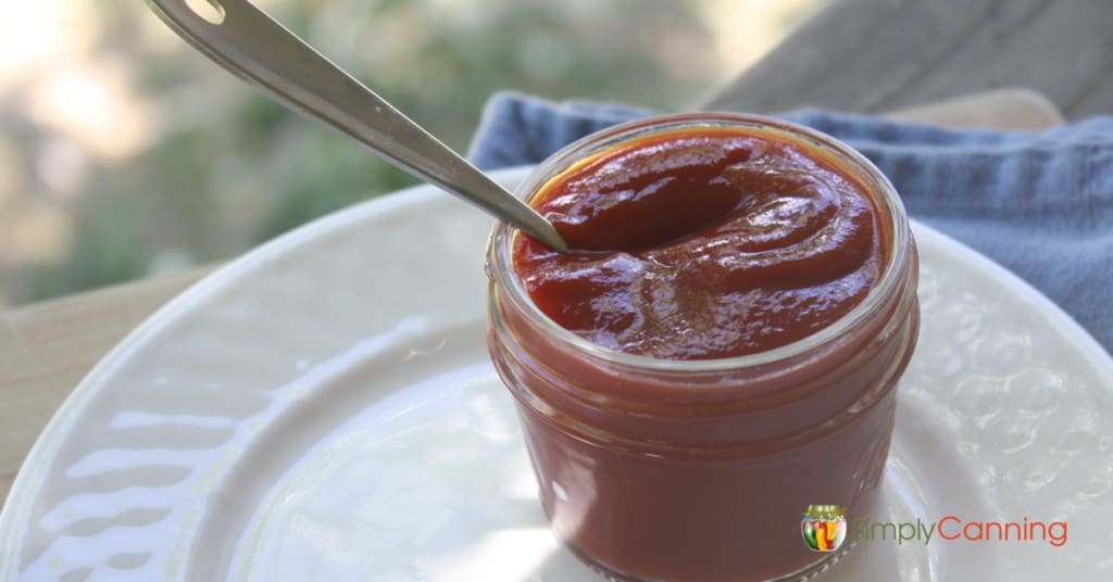 A spoon in a small canning jar filled with thick ketchup.