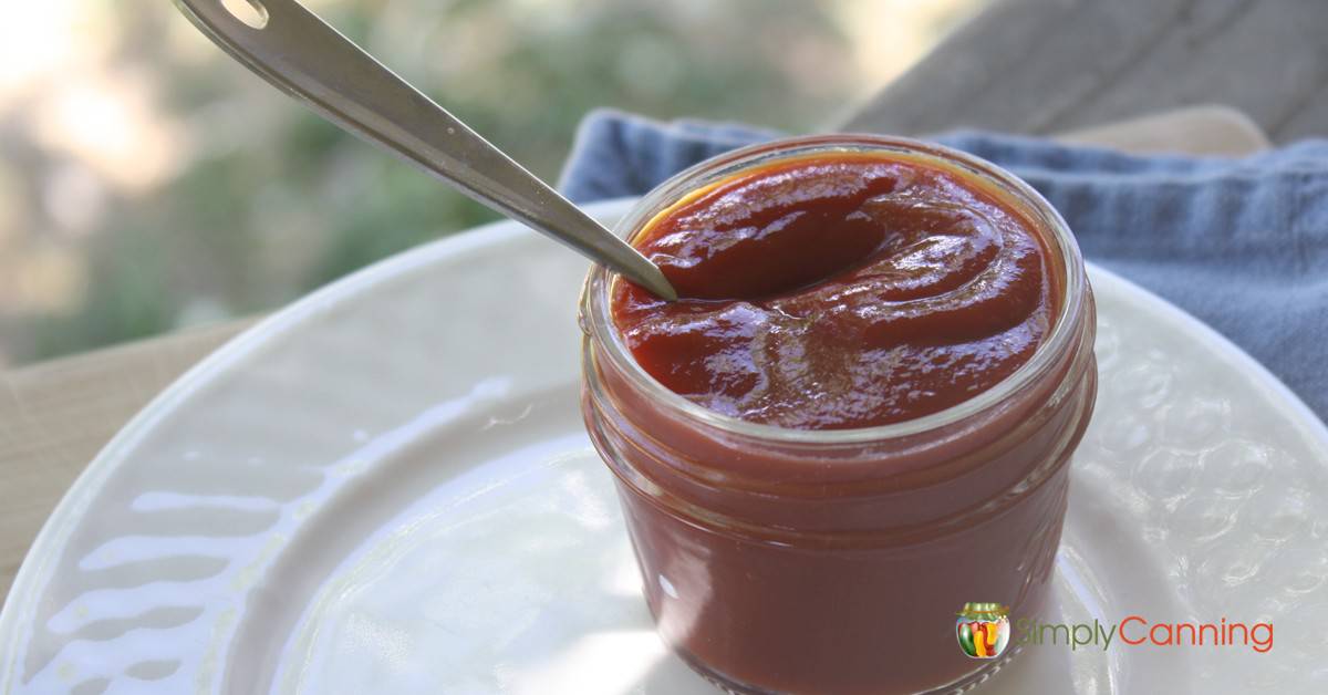 A spoon in a small canning jar filled with thick ketchup.