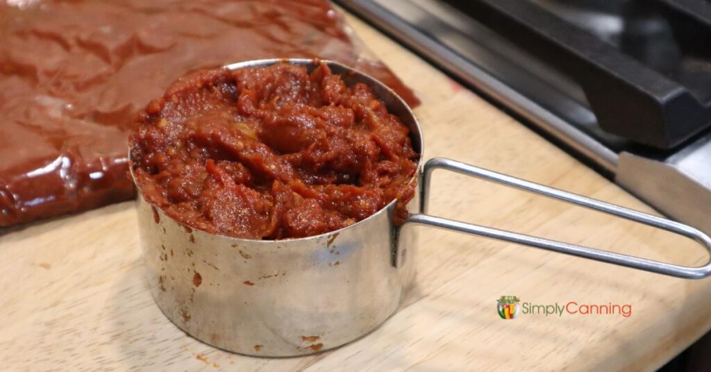 Metal measuring cup filled with thick rich homemade tomato paste.