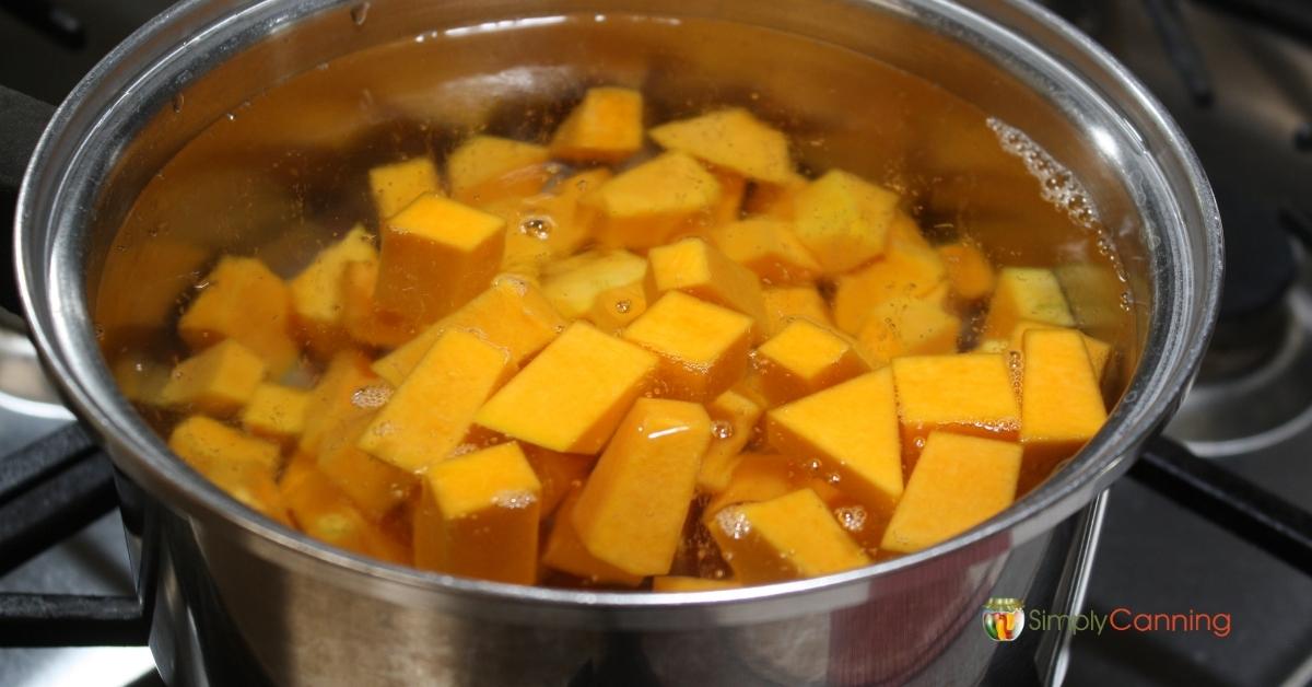 Large pot of chopped butternut squash coming to a boil.
