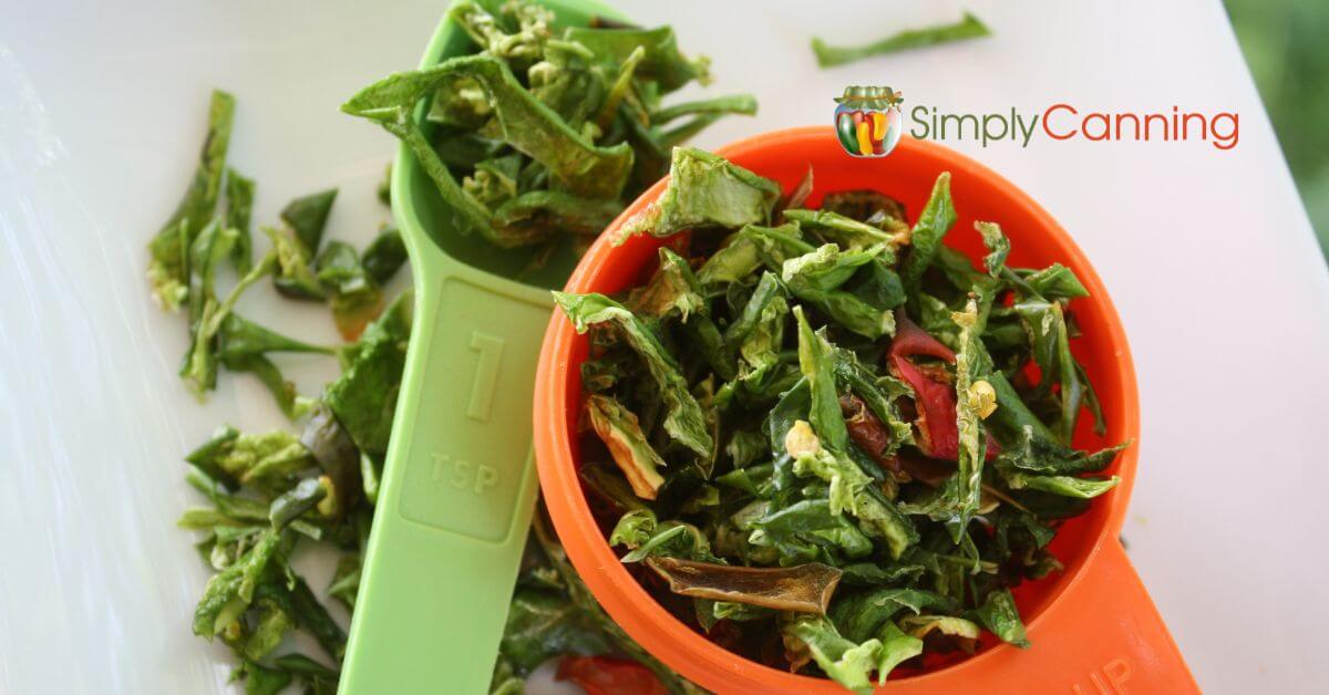 chopped dehydrated green and red peppers, in colorful orange and green measuring cup and spoon.