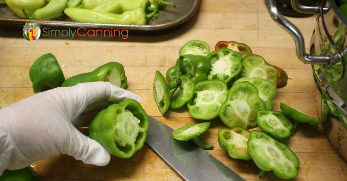 Green pepper with the top cut off, insides not yet taken out, several pepper tops lying to the side. 