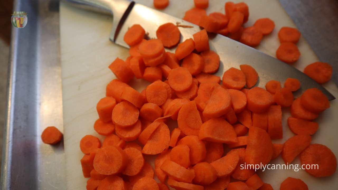 sliced carrots and a large knife sitting on a white cutting board.  