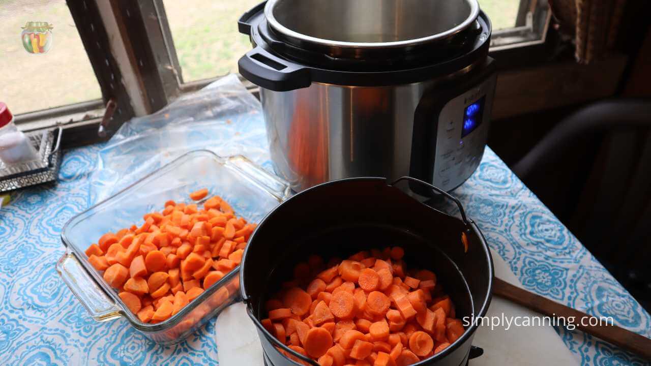 Instant pot with the insert filled with chopped carrots ready to be blanched and a clear square pan sitting on the table with already blanched carrots. 
