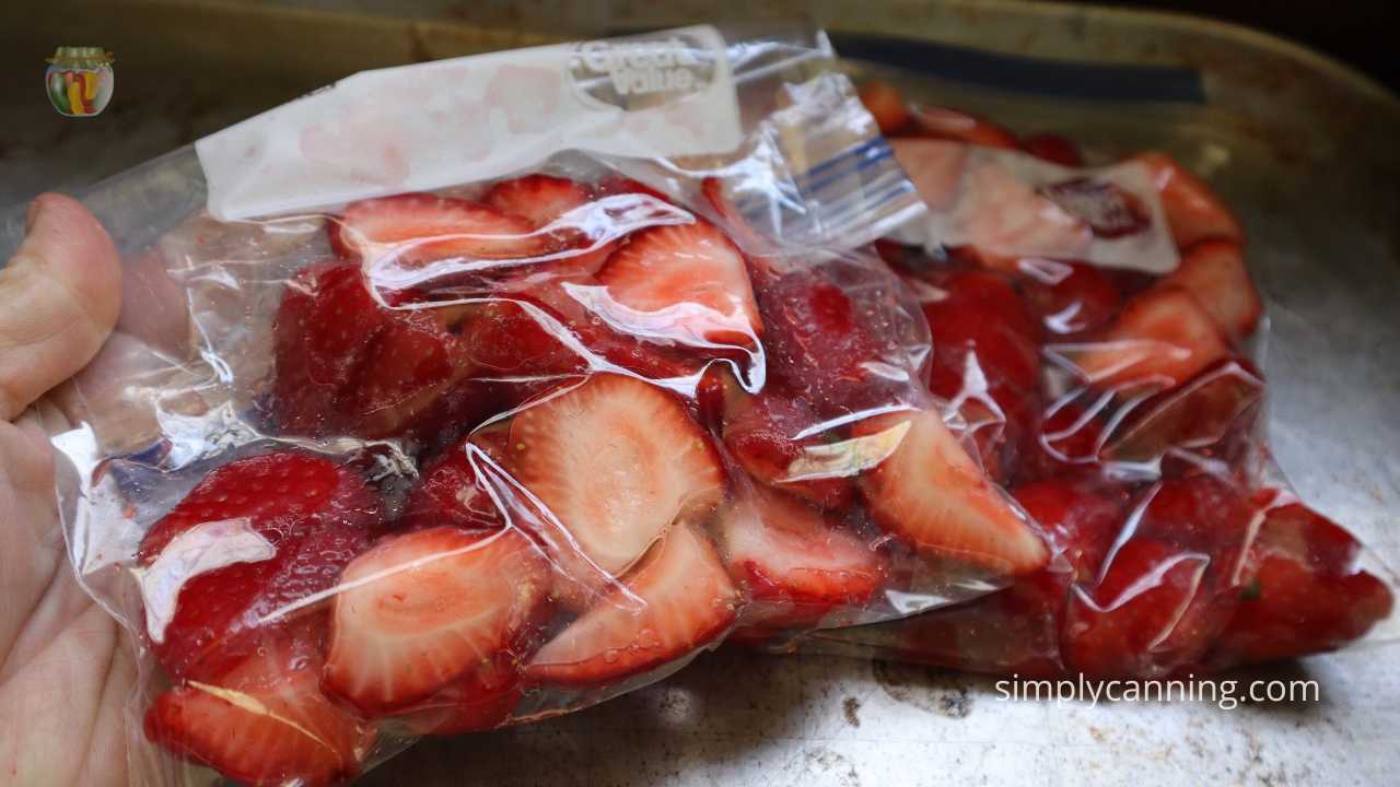 hand holding quart size freezer bag with strawberries ready to go in the freezer.  