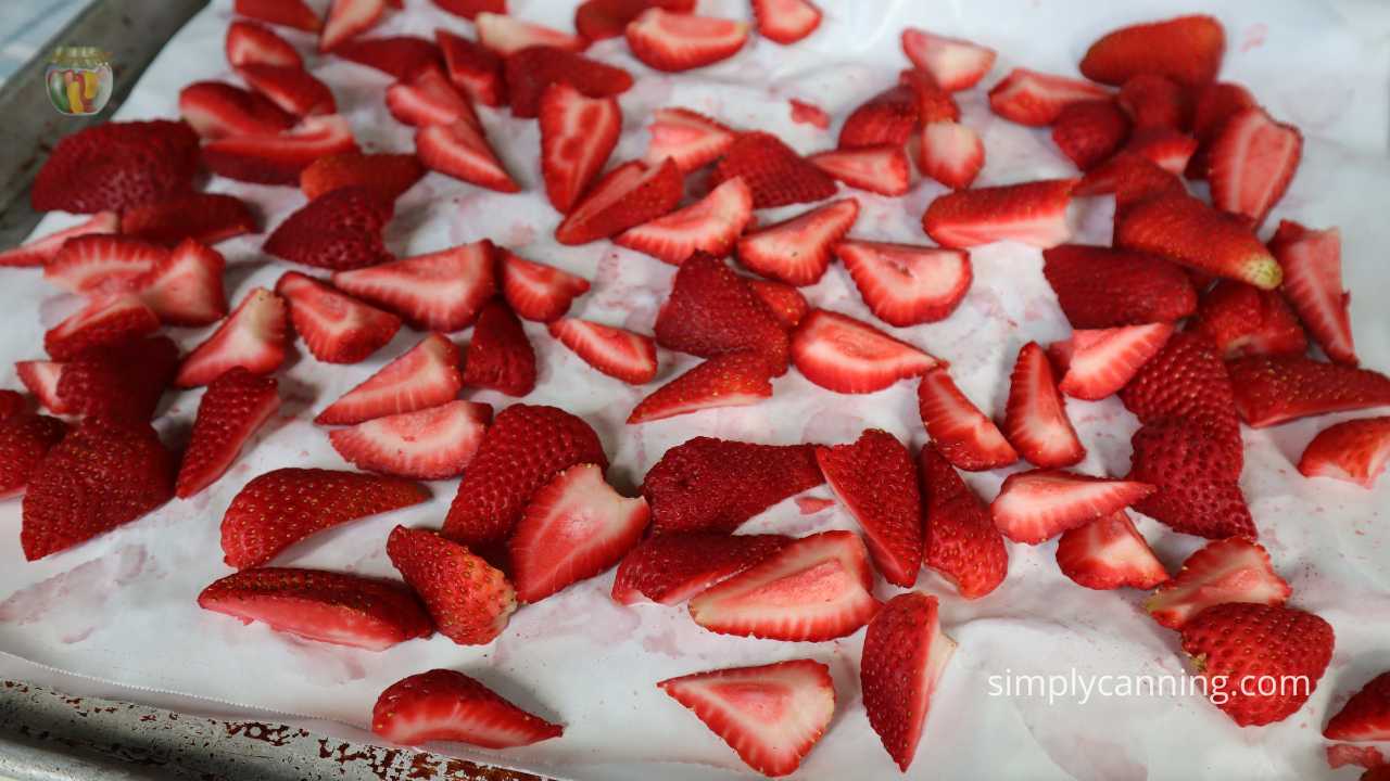 Freezer paper lined baking tray with cut strawberries laid out in a single layer. 