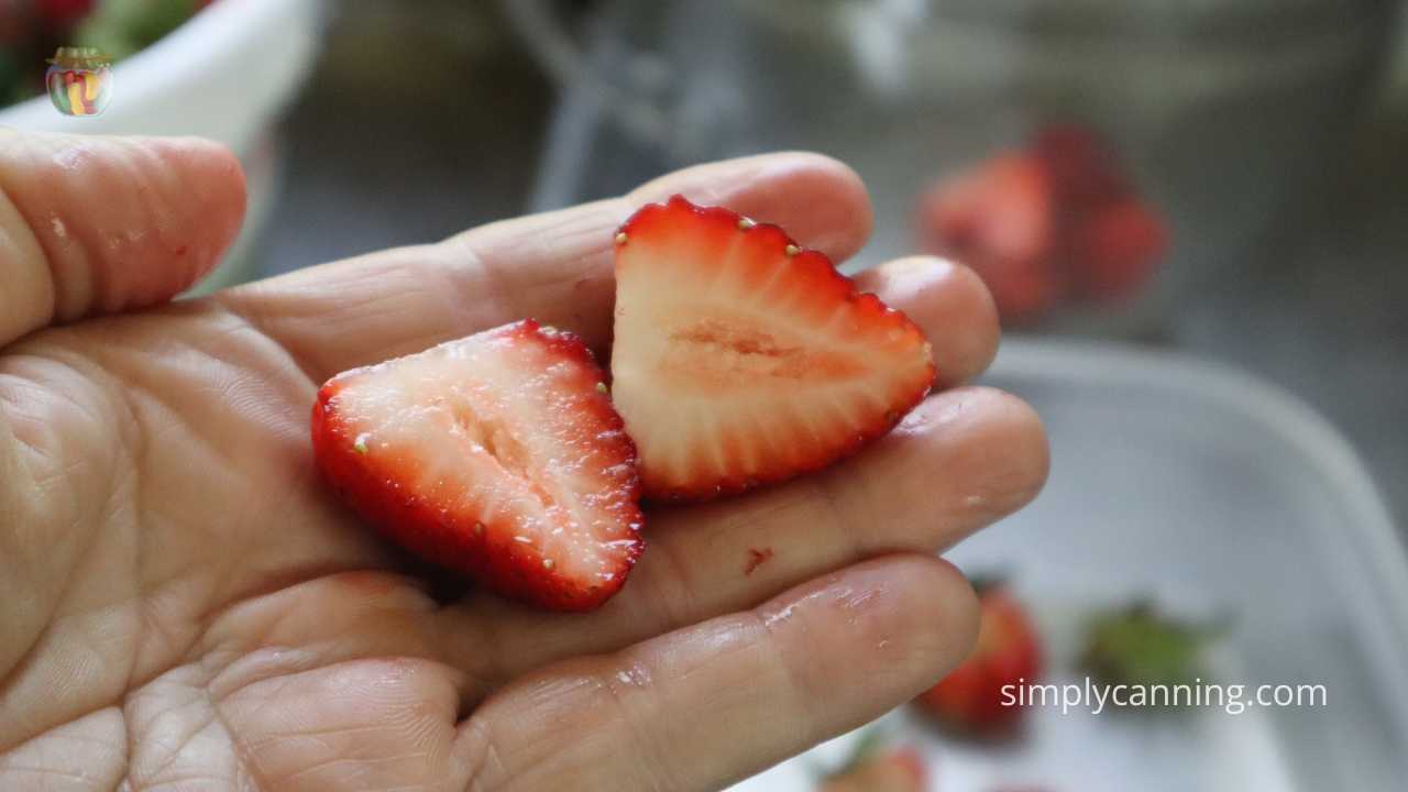 Hand holding a strawberry cut in half.