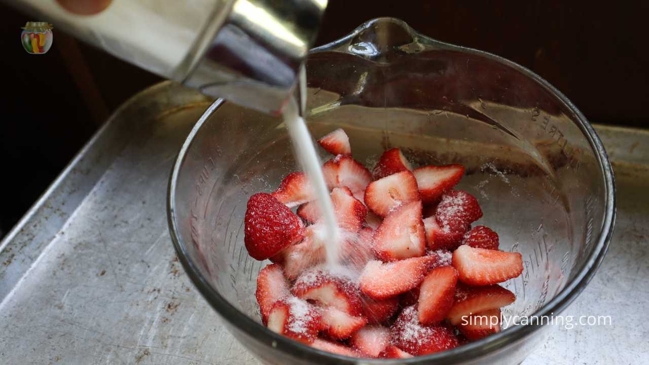 Pouring sugar over strawberries in a glass bowl. 