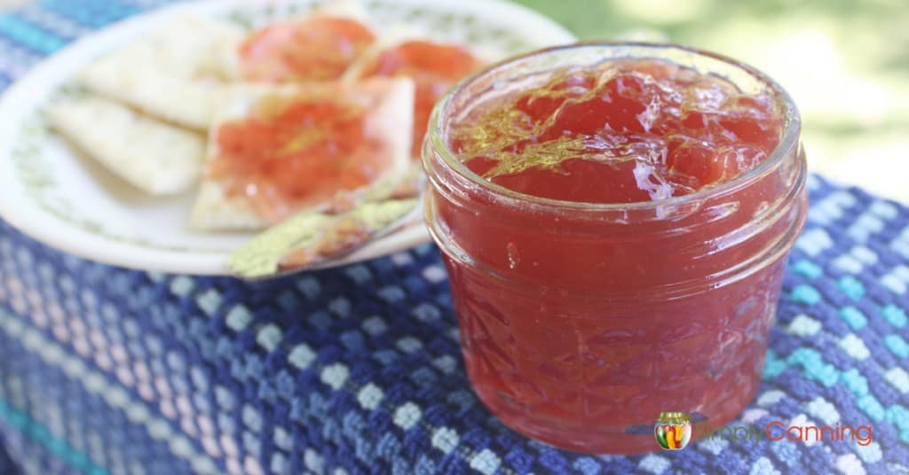 An open jar of homemade jam sitting next to a plate of crackers spread with jam.