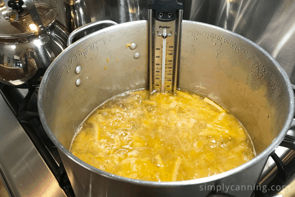 A candy thermometer on the side of a boiling pot of jam.