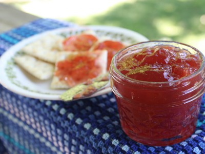 An open jar of red jam or jelly sitting next to a plate of crackers.