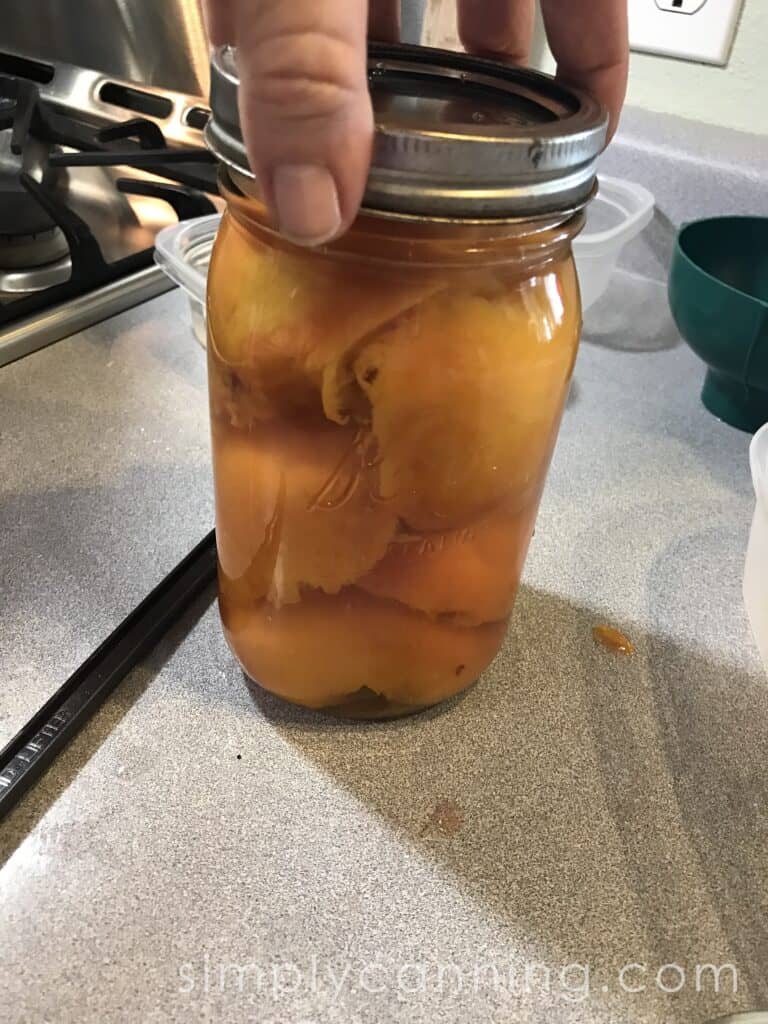 Lifting a jar that's filled with peaches and ready to go into the canner.