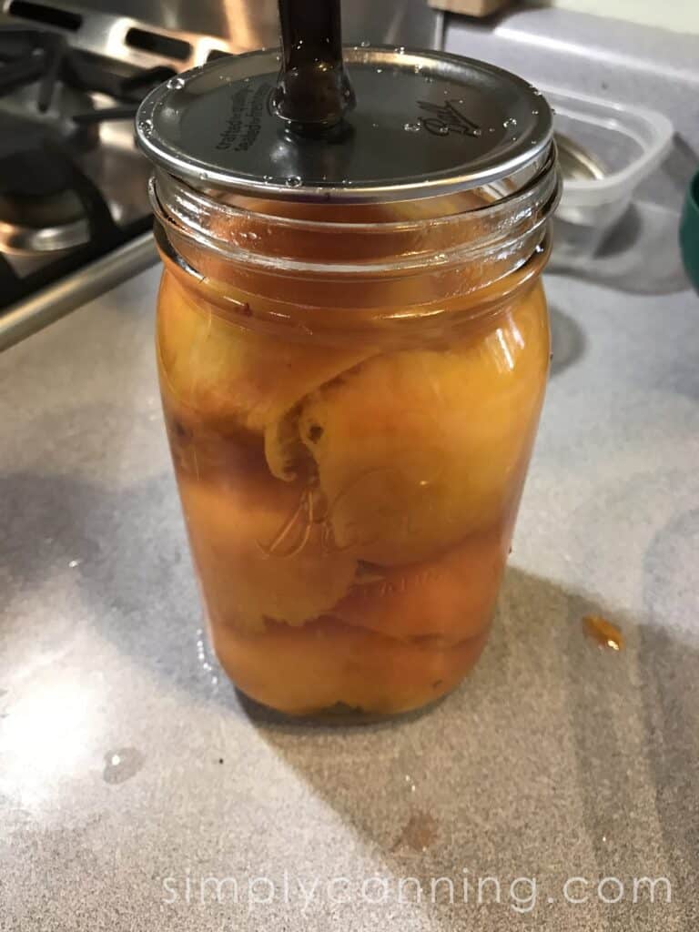 Placing the flat lid on a canning jar that's filled with peaches and syrup.