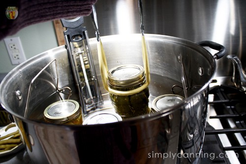 Lifting a jar of pickles from the water bath canner with the thermometer still submerged into the water of the canner.