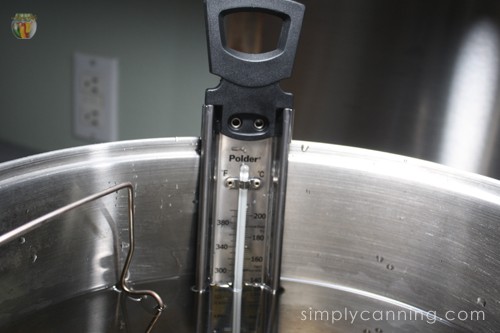 Closeup of the candy thermometer that is submerged in the water of the canner.