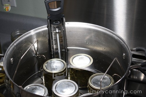 A thermometer stuck into a water bath canner filled with pickle jars.