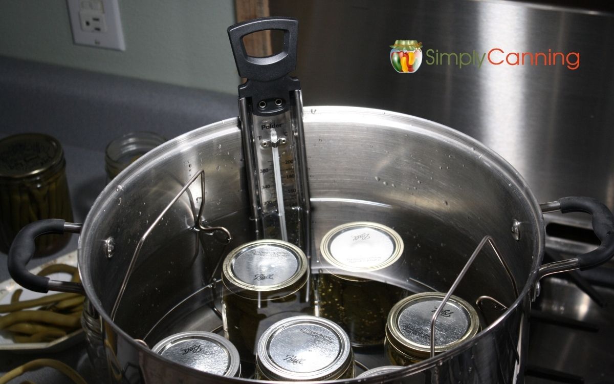 Canning Jars in a water bath canner with a thermometer checking temperature. 
