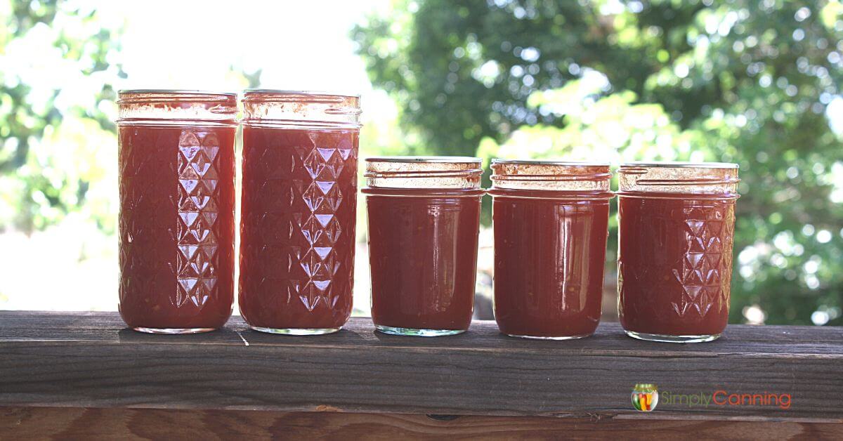Half pint jars of tomato juice lined up on the deck railing. 