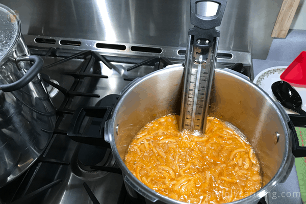 Pot of orange marmalade cooking on the stove with a thermometer to check for gelling point.