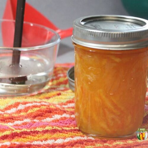 A jar of orange marmalade with various canning supplies around it.