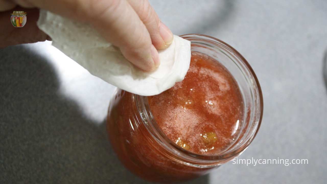top view of wiping the rim of a jar just filled with jam.
