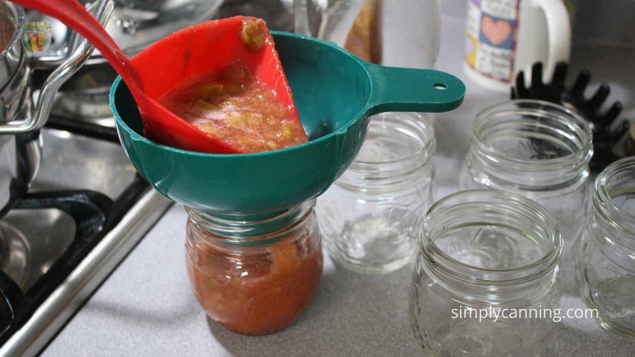 putting jam in a jelly jar on the counter with a canning funnel and red ladle. 