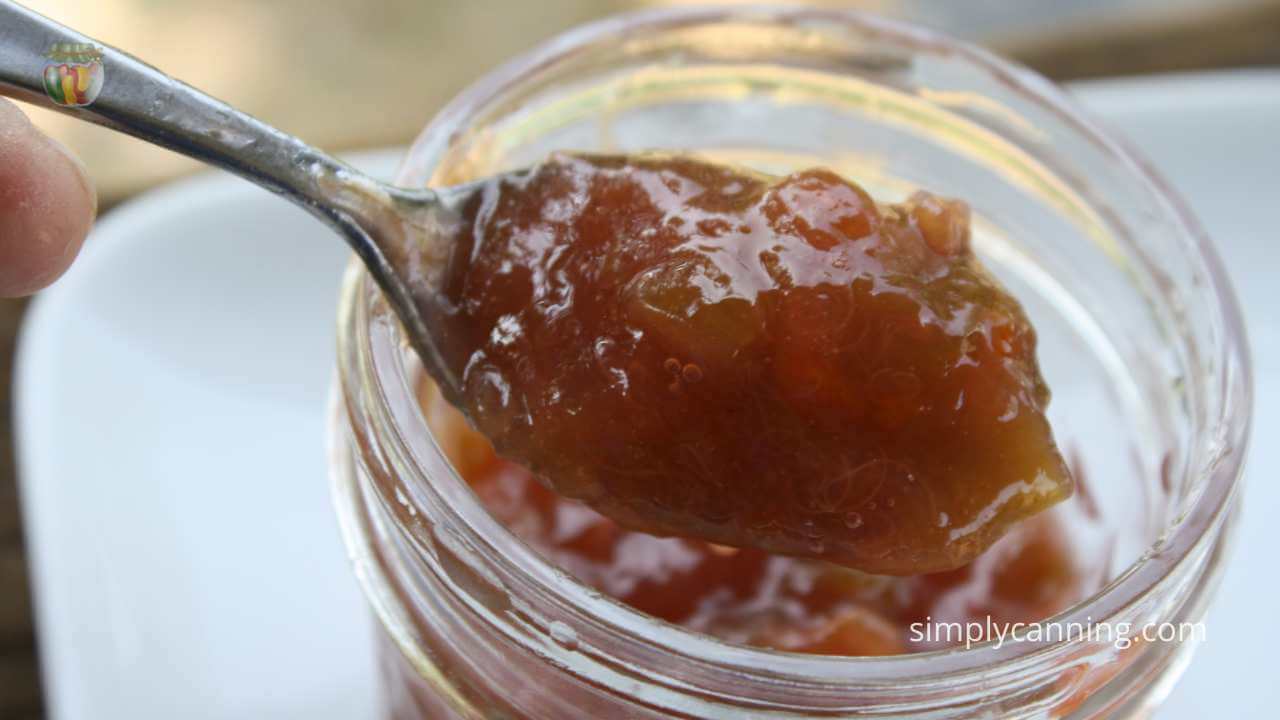 spooning orange rhubarb jam out of a small jelly jar. 