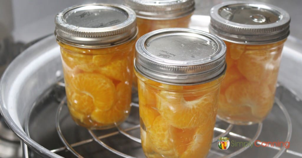 Jars of orange segments sitting on a steam canner rack.