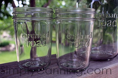 Clear empty glass Orchard Road canning jars sitting outside on the wooden railing.