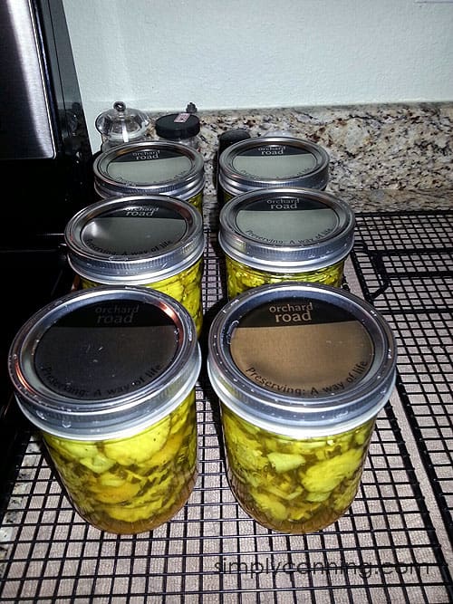 Six Orchard Road canning jars packed with pretty pickles and sitting on top of a rack to cool.