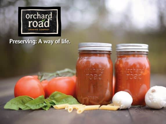 Two jars of tomato sauce surrounded by individual ingredients for making sauce.