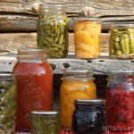Jars of colorful home canned food sitting in front of a rustic wooden background.