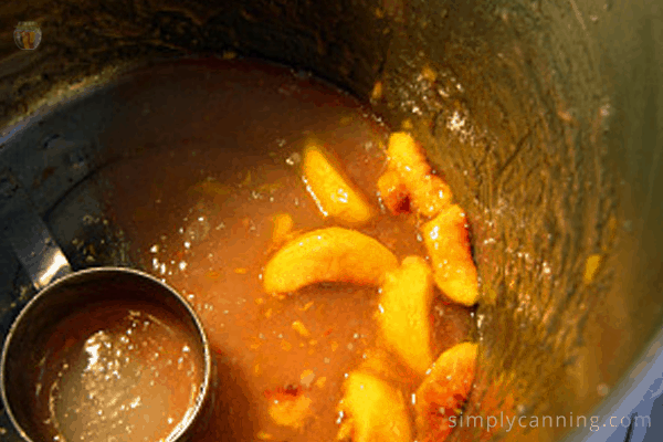 The last of the thickened juice and peach slices at the bottom of the pot with a measuring cup sitting in it.