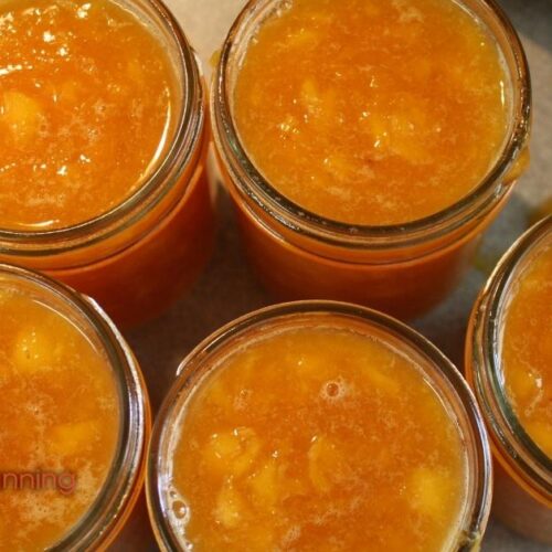 Top down view of 5 opened half pint jars of peach pineapple jam.