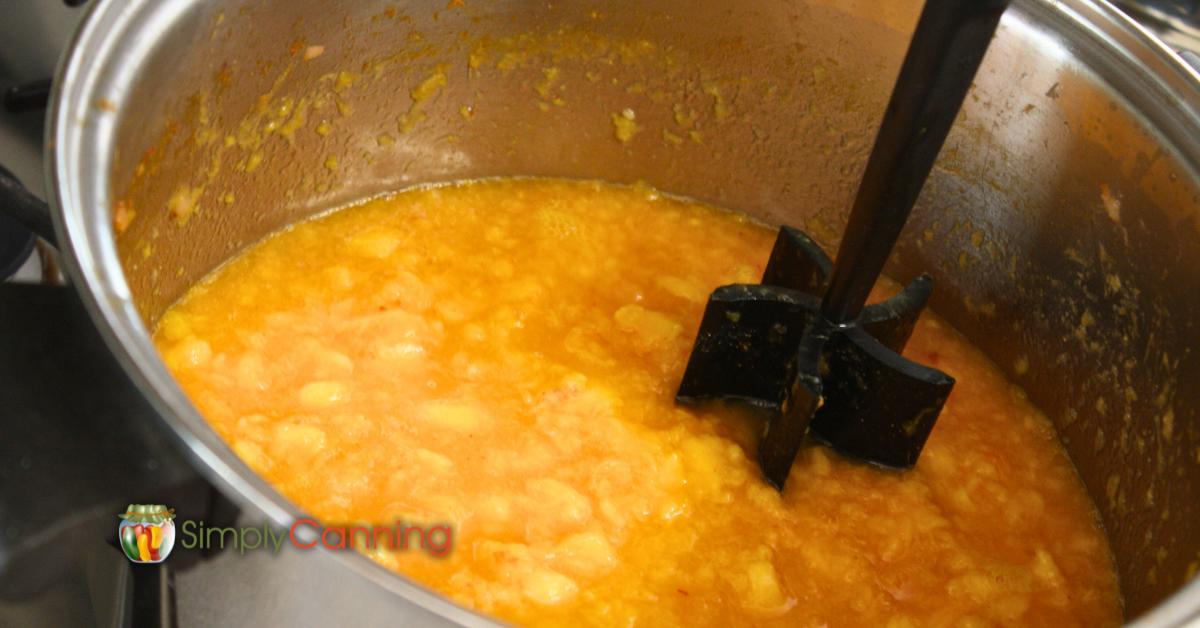 Peach and Pineapple jam being stirred in the pot with a black masher.