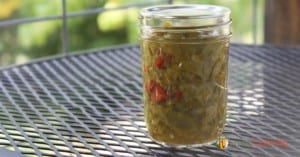 A jar of green peppers with a few red pepper pieces included in it.