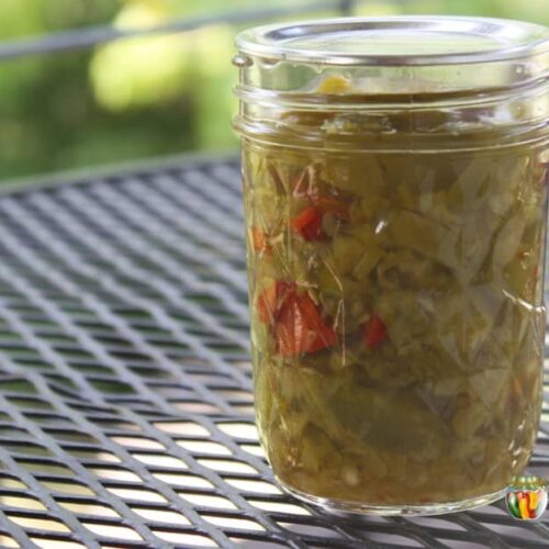 A jar of green peppers with a few red pepper pieces included in it.